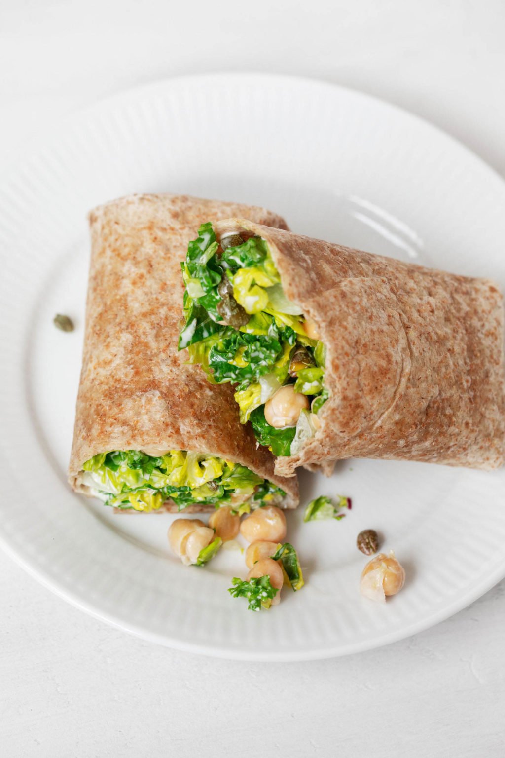 A whole grain wrap has been stuffed with a vegan chickpea Caesar salad. It rests on a white serving plate.