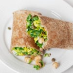 A whole grain wrap has been stuffed with a vegan chickpea Caesar salad. It rests on a white serving plate.