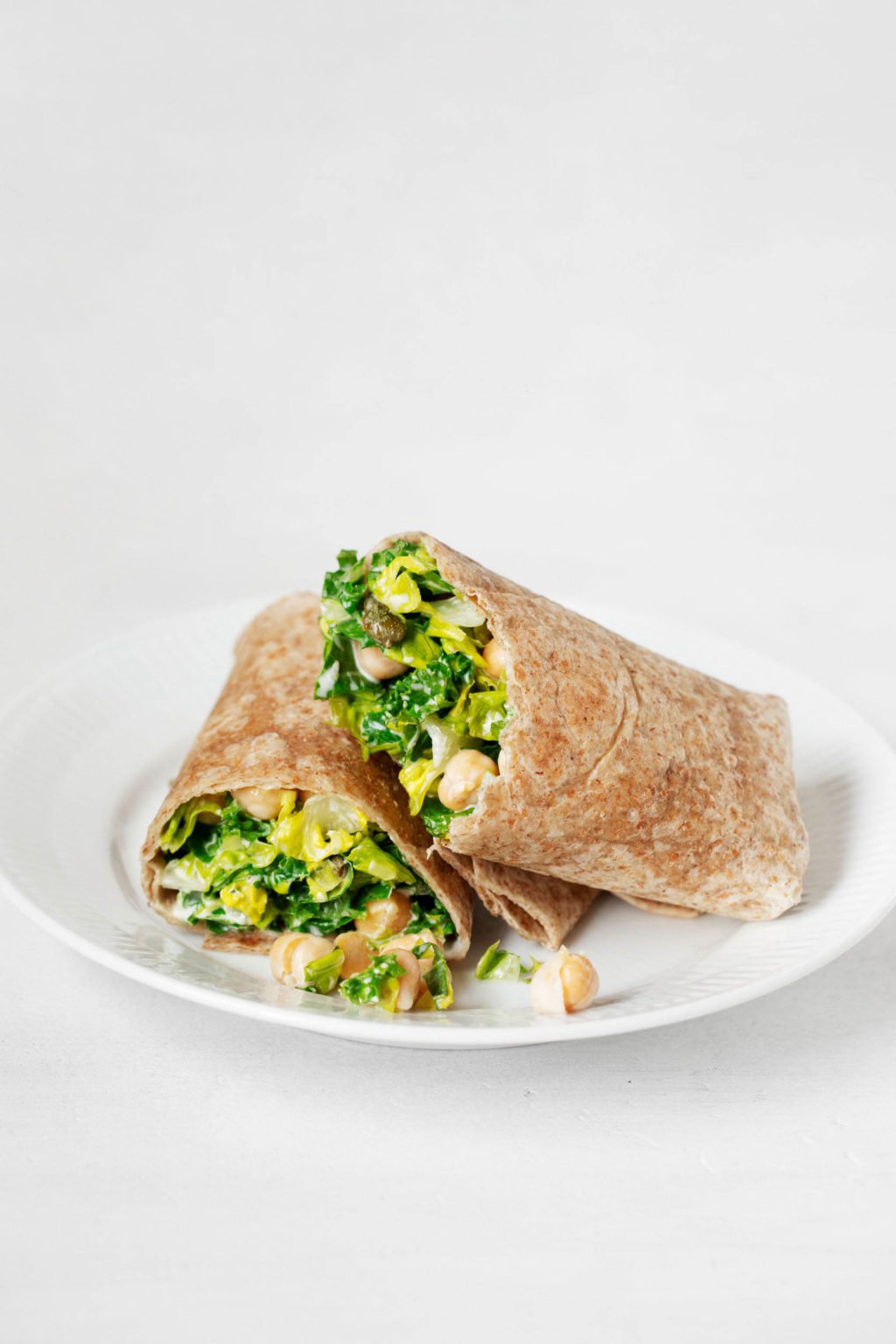 A cut wrap with greens and chickpeas has been assembled on a serving plate. The plate is resting on a white surface.