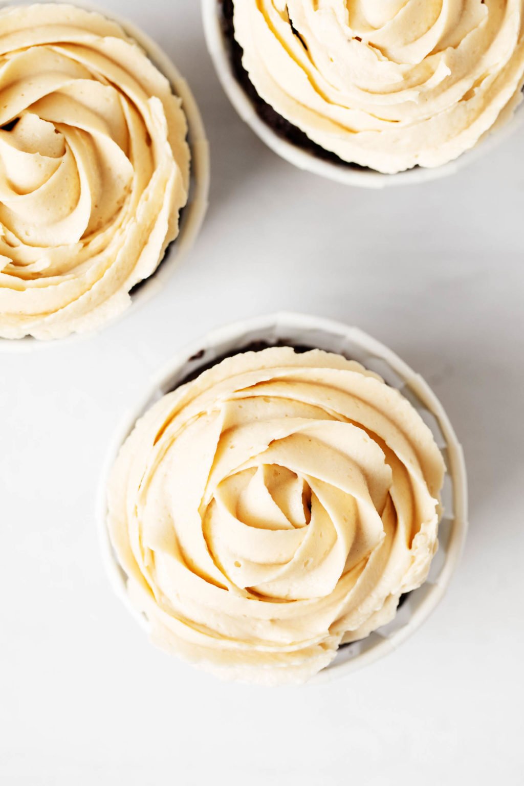 The top of a few cupcakes, which have been piped with a light-colored buttercream frosting.