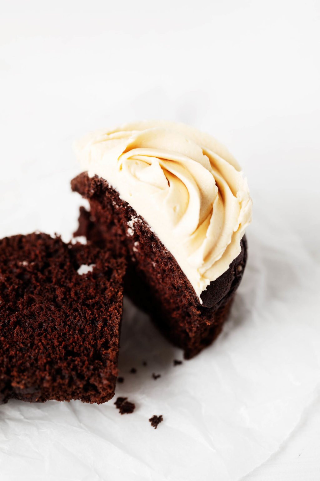 A chocolate peanut butter cupcake has been sliced neatly in half. It's resting on a small dessert plate.