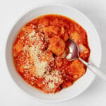 A white bowl is being used to hold a cozy vegan tomato bread soup, topped with plant-based parmesan cheese.