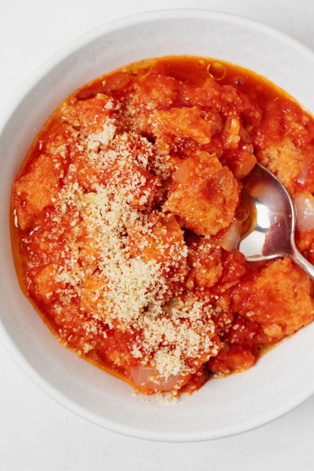 An overhead image of a rustic, Italian soup with tomatoes and leftover bread. The soup is topped with plant-based parmesan cheese.