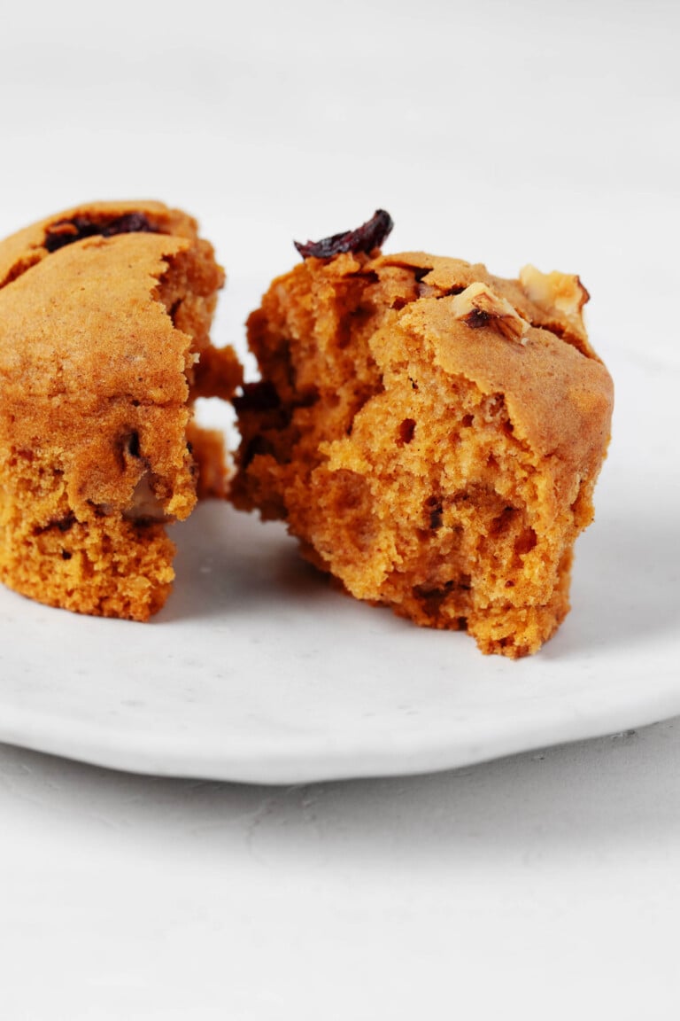 The cross-section of a vegan pumpkin muffin is pictured. The muffin rests on a small white serving plate.