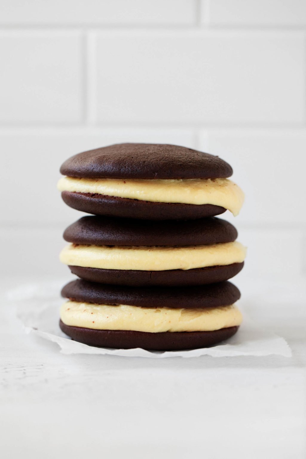 A sideways photograph of a neat stack of vegan Halloween whoopie pies, made with soft chocolate cookies and pumpkin cream.