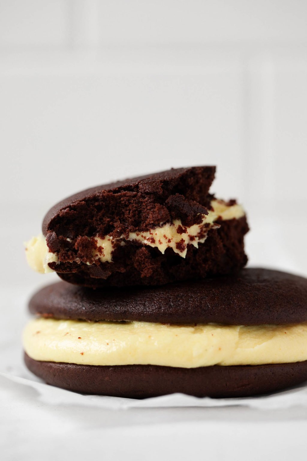 A photograph of a vegan chocolate and pumpkin whoopie pie, just bitten into and stacked on top of another pie.