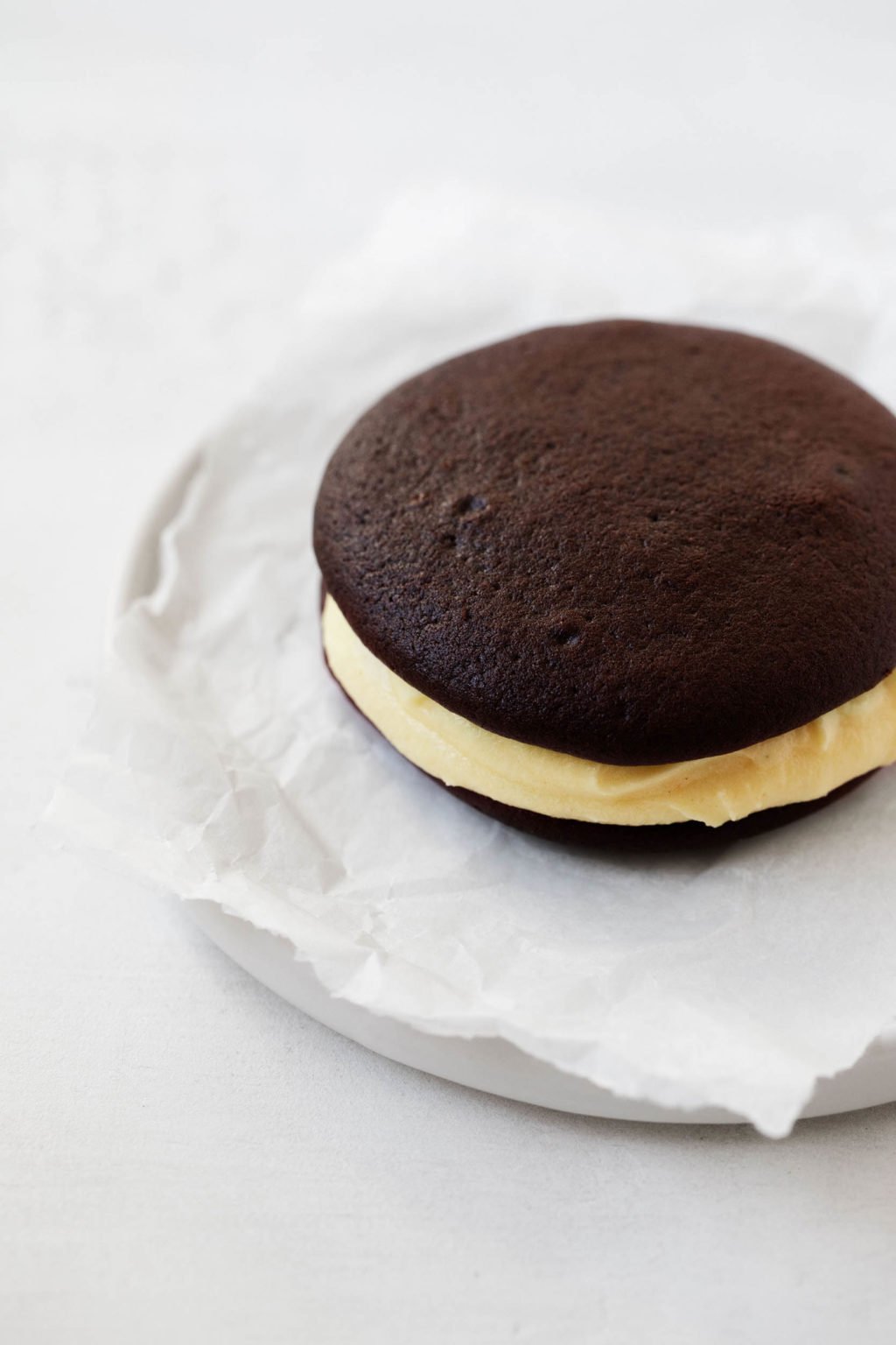 A chocolate and pumpkin vegan whoopie pie, served on a small dessert plate with a crumpled sheet of parchment.