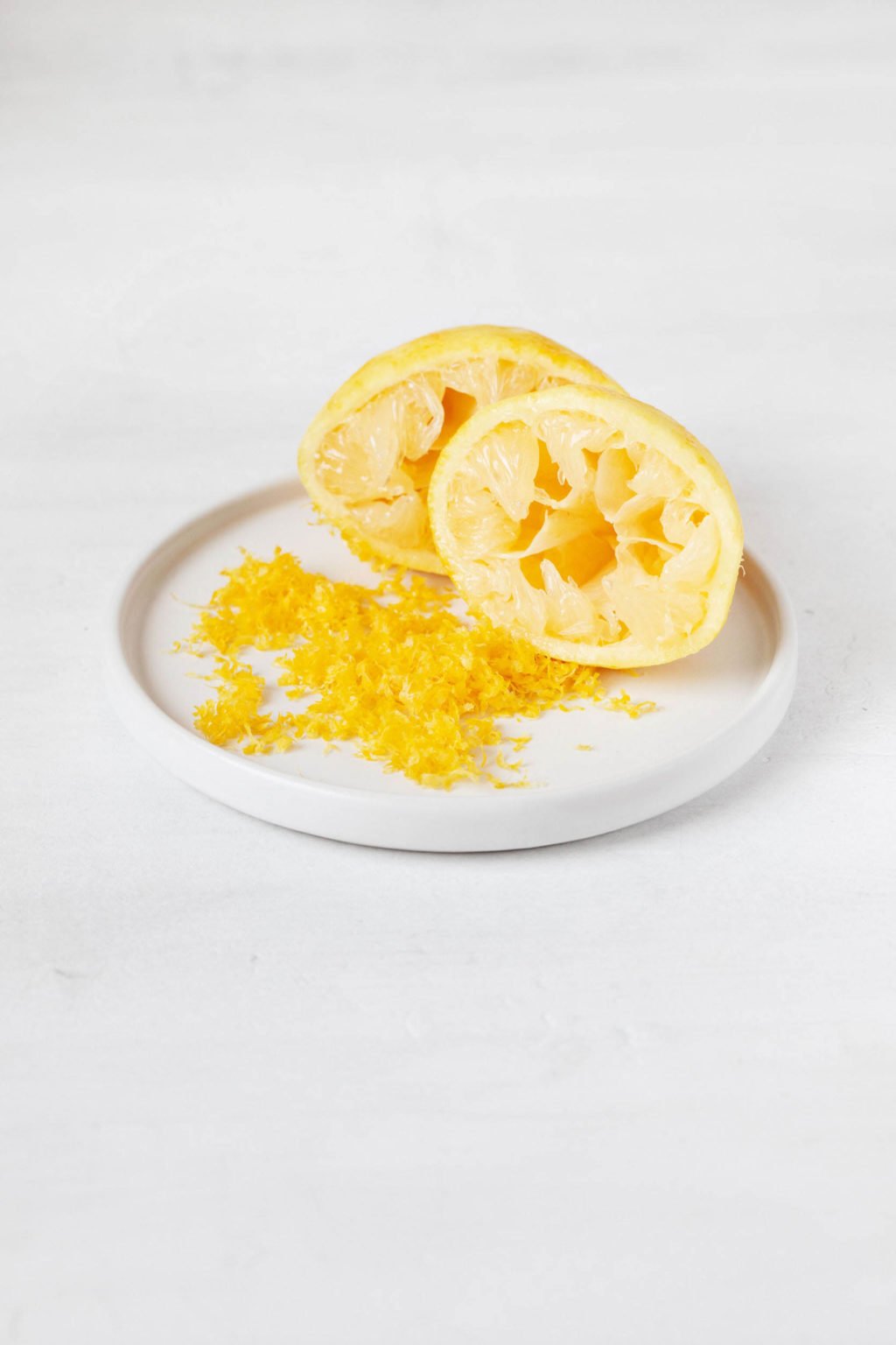 A zested lemon rests on a small, round white plate. 