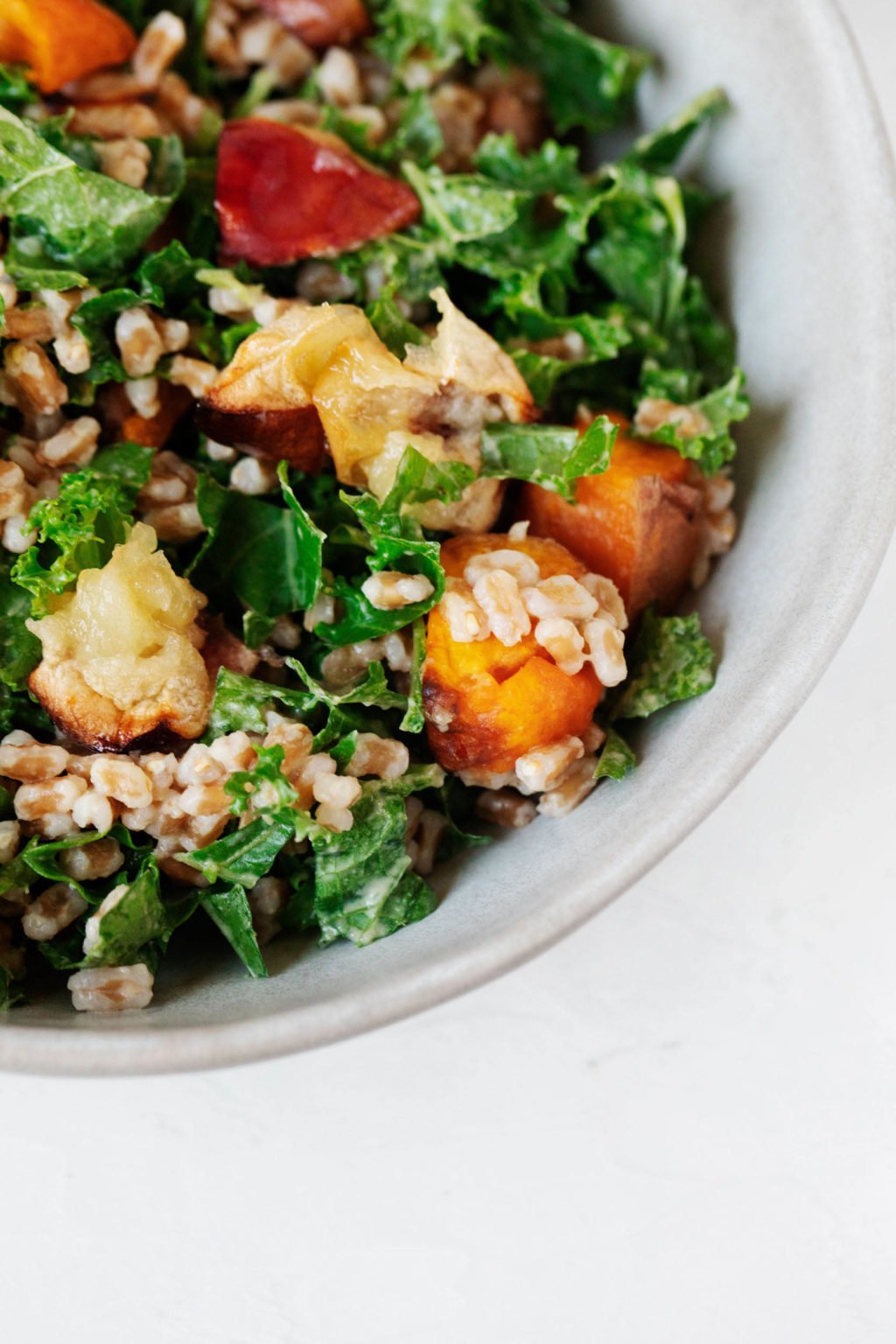 An overhead image of roasted apples and root vegetables, farro, kale, and a creamy dressing.