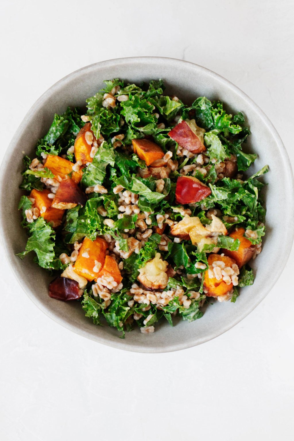 An overhead image of a plant-based salad with roasted sweet potatoes and apples. It's served in a white salad bowl and sitting on a white surface.