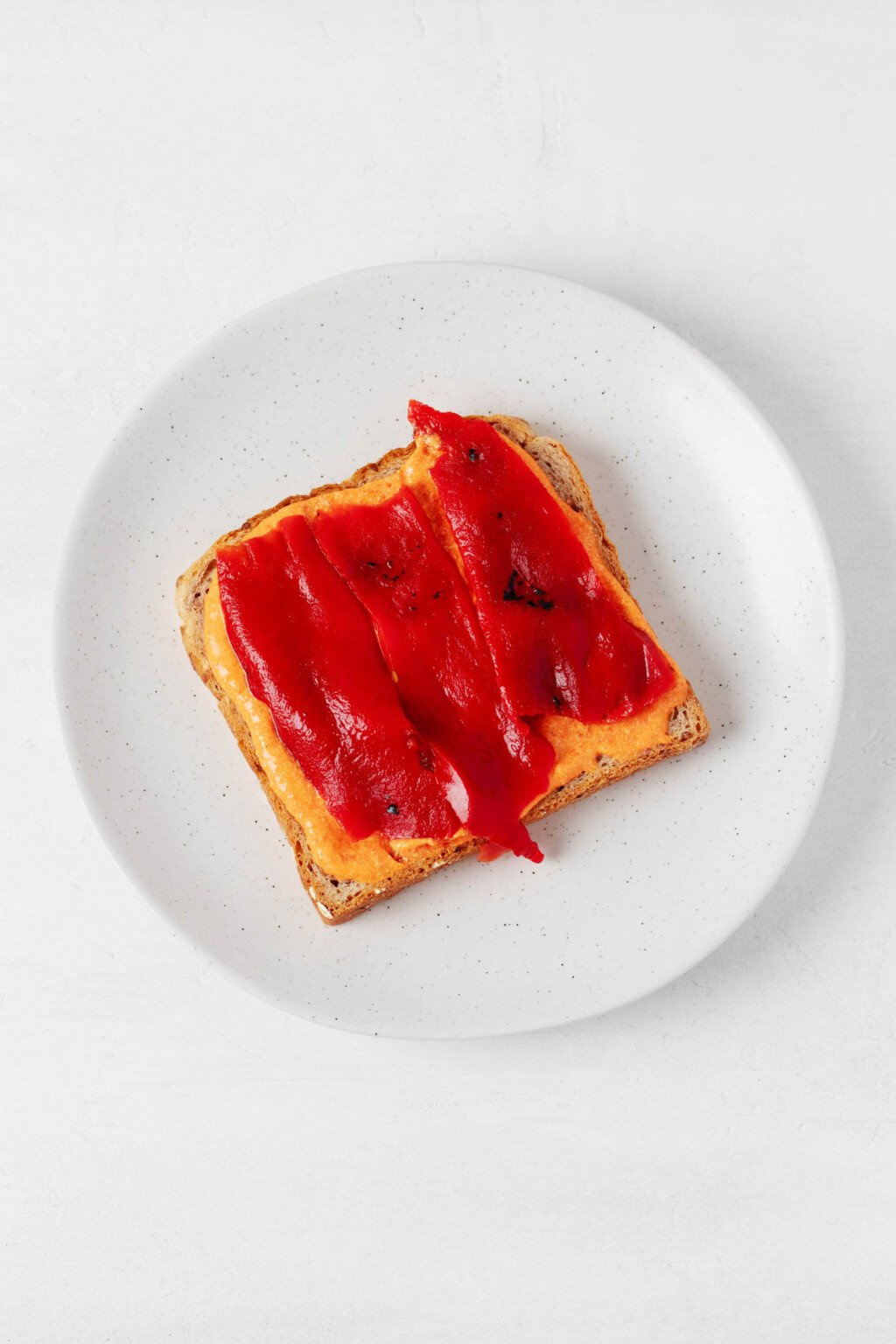 Red pepper strips and a sweet potato spread are layered onto a piece of bread.