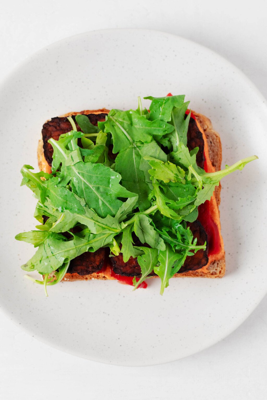 Green arugula is being added to a sandwich.