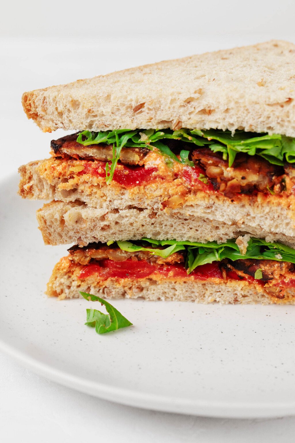 A cross section of a sandwich that has been prepared with tempeh, greens, red pepper, and a sweet potato spread.