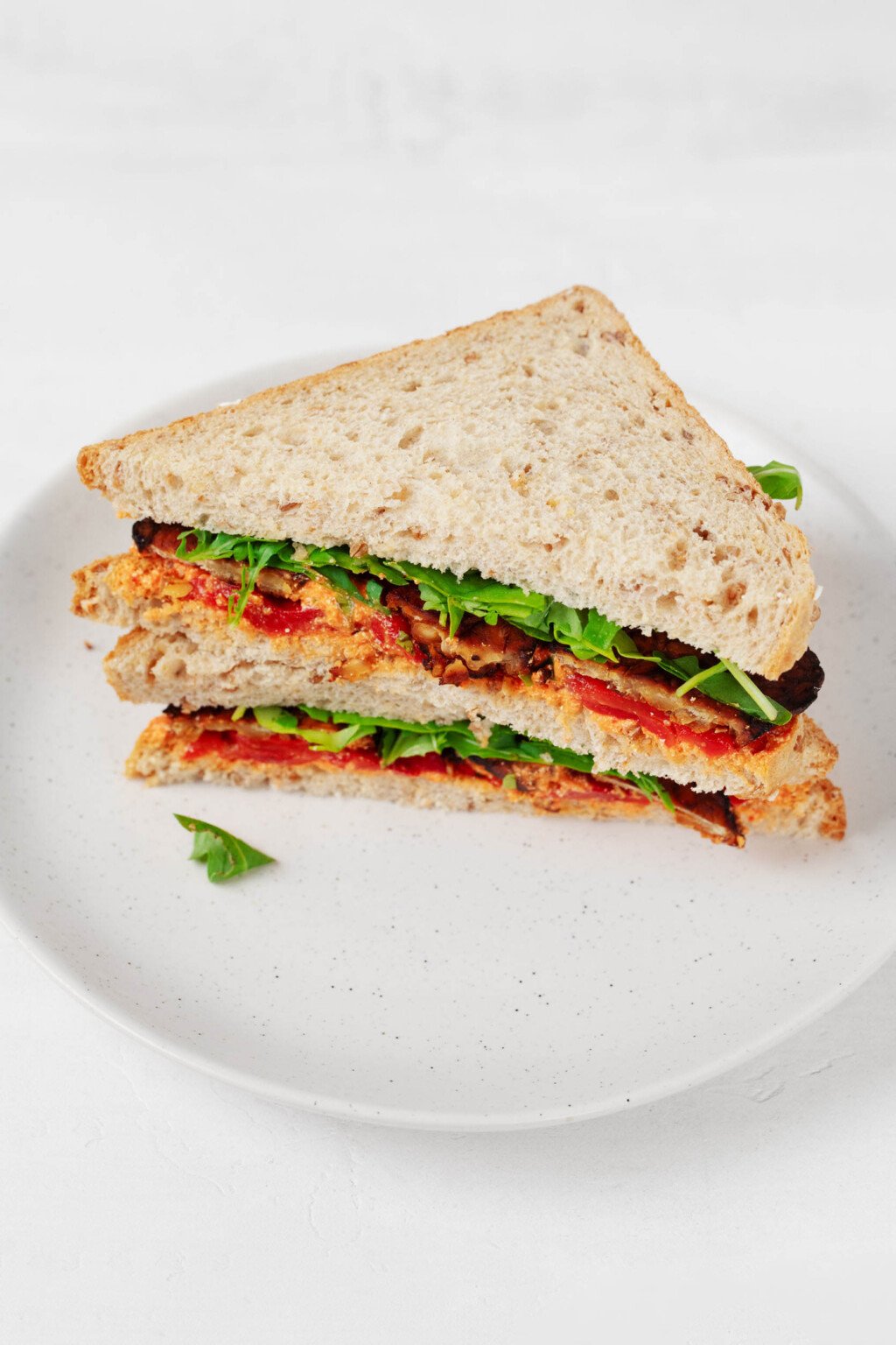 A cross section of a sandwich that has been prepared with tempeh, greens, red pepper, and a sweet potato spread.