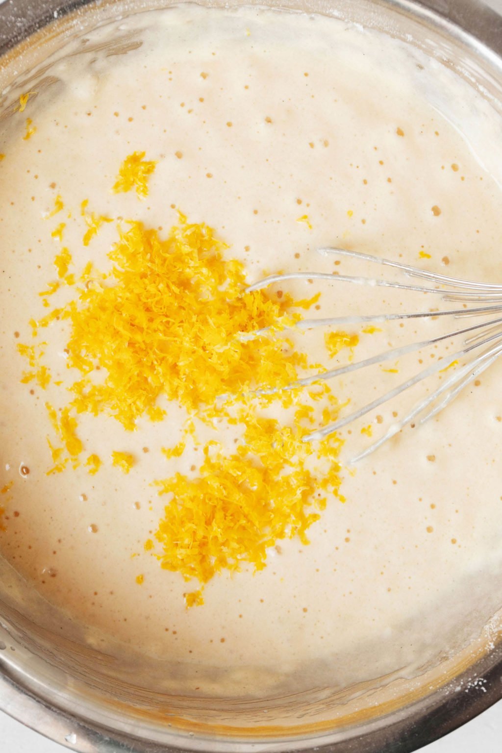 A pale, yellow batter for baking is being whisked with bright yellow lemon zest.