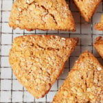 A few pumpkin oat scones, decorated with sparkling sugar, are resting on a wire cooling rack.