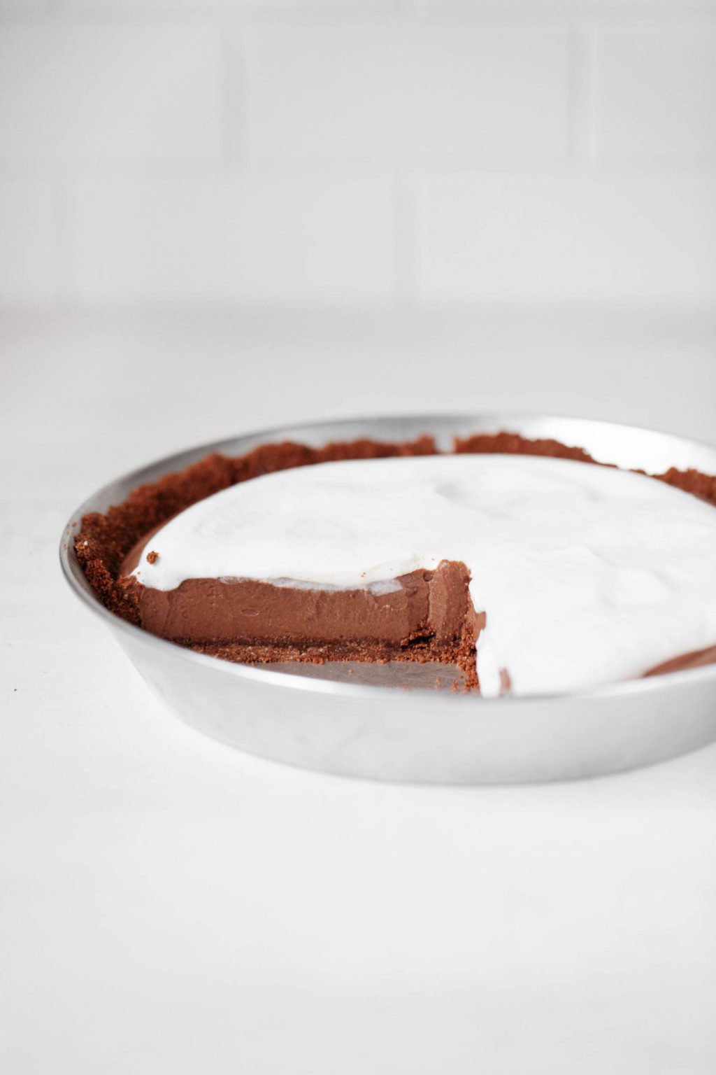 A vegan chocolate mousse pie is held in a silver pie plate. It rests on a white surface.