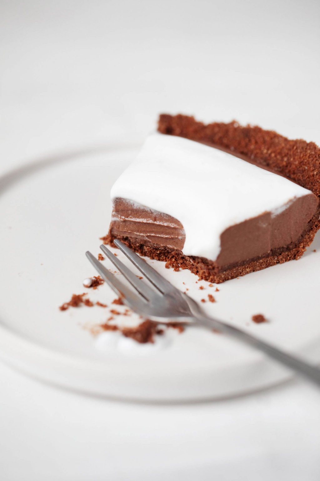 A slice of chocolate mousse pie is being eaten. It rests on a white dessert plate with a silver fork nearby.