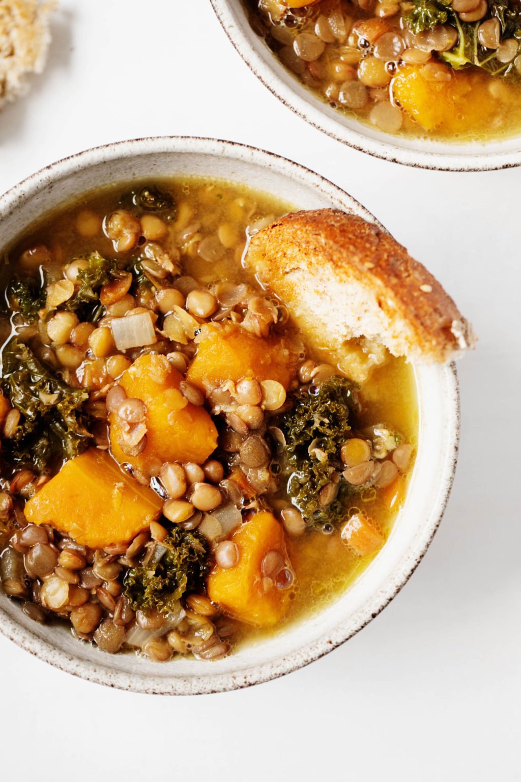 A close up photograph of a hearty vegan legume and vegetable stew, with bread poking out of the round serving bowl.