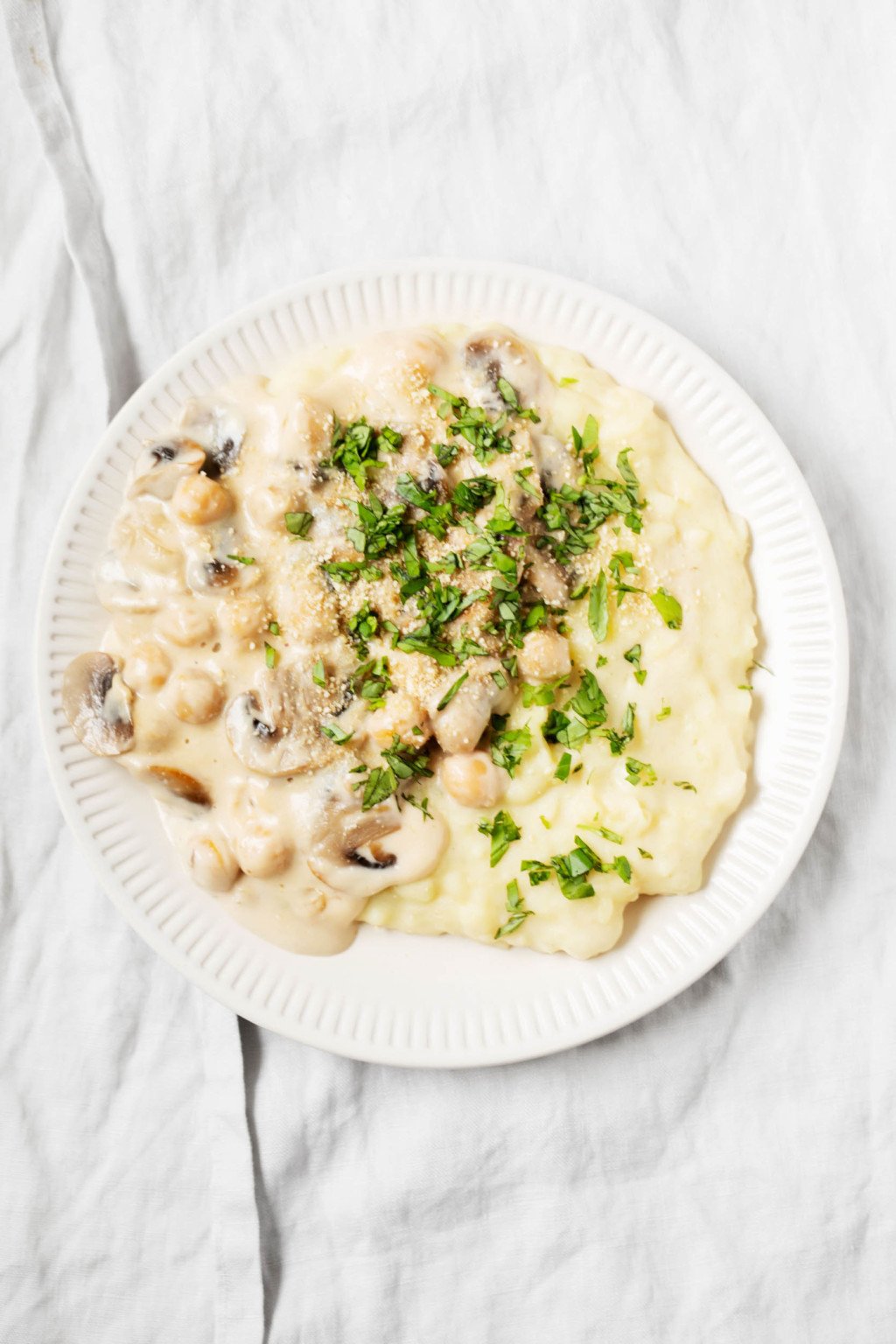 A round, fluted ceramic plate has been piled with rustic, vegan creamy chickpeas & mashed potatoes.