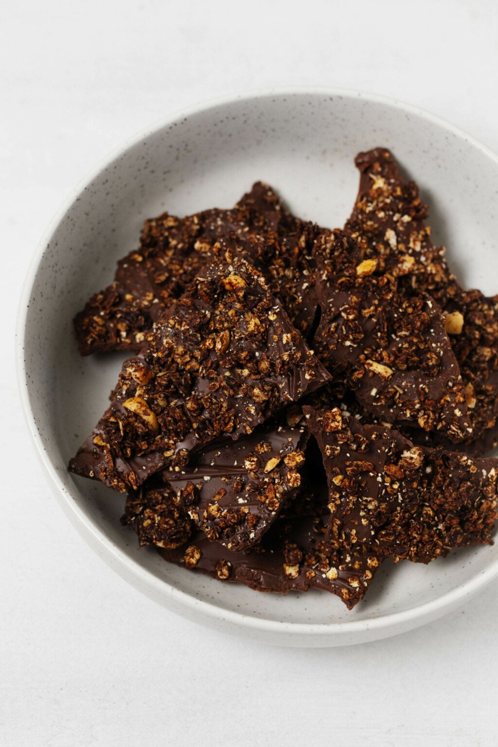 A round ceramic bowl is filled with vegan granola chocolate bark pieces.