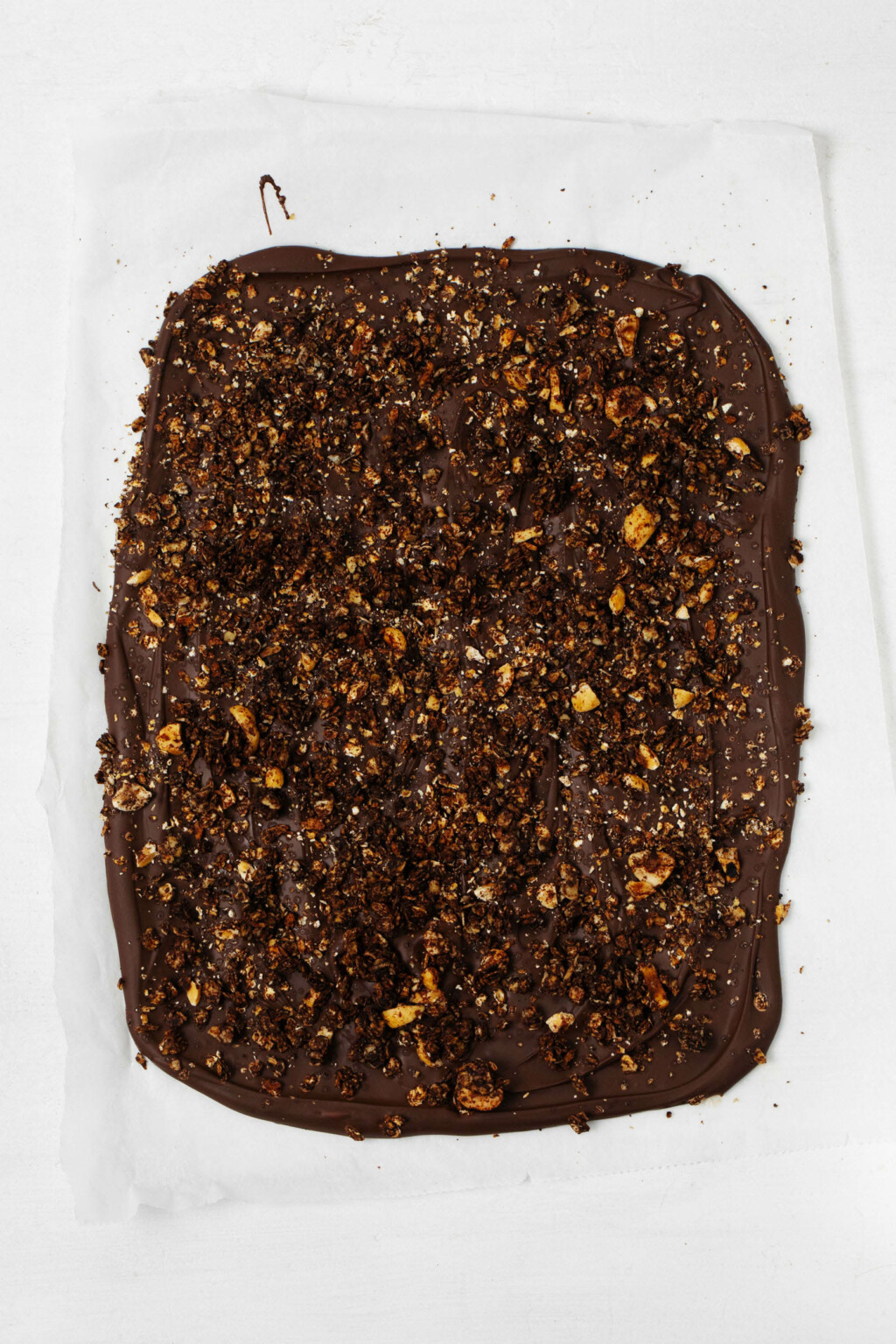 An overhead image of a baking sheet that has been covered with vegan dark chocolate bark. the bark is studded with granola, dried fruit, and chopped walnuts.
