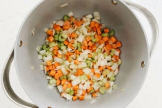 Onion, carrot, and celery is being sautéed in a large pot.