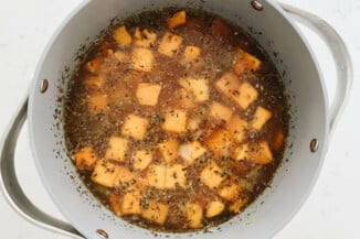 Butternut squash, vegetable broth, and herbs are simmering in a gray colored soup pot.