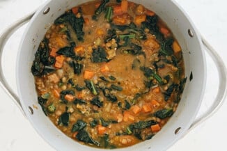 A gray soup pot is filled with a butternut kale & lentil soup.