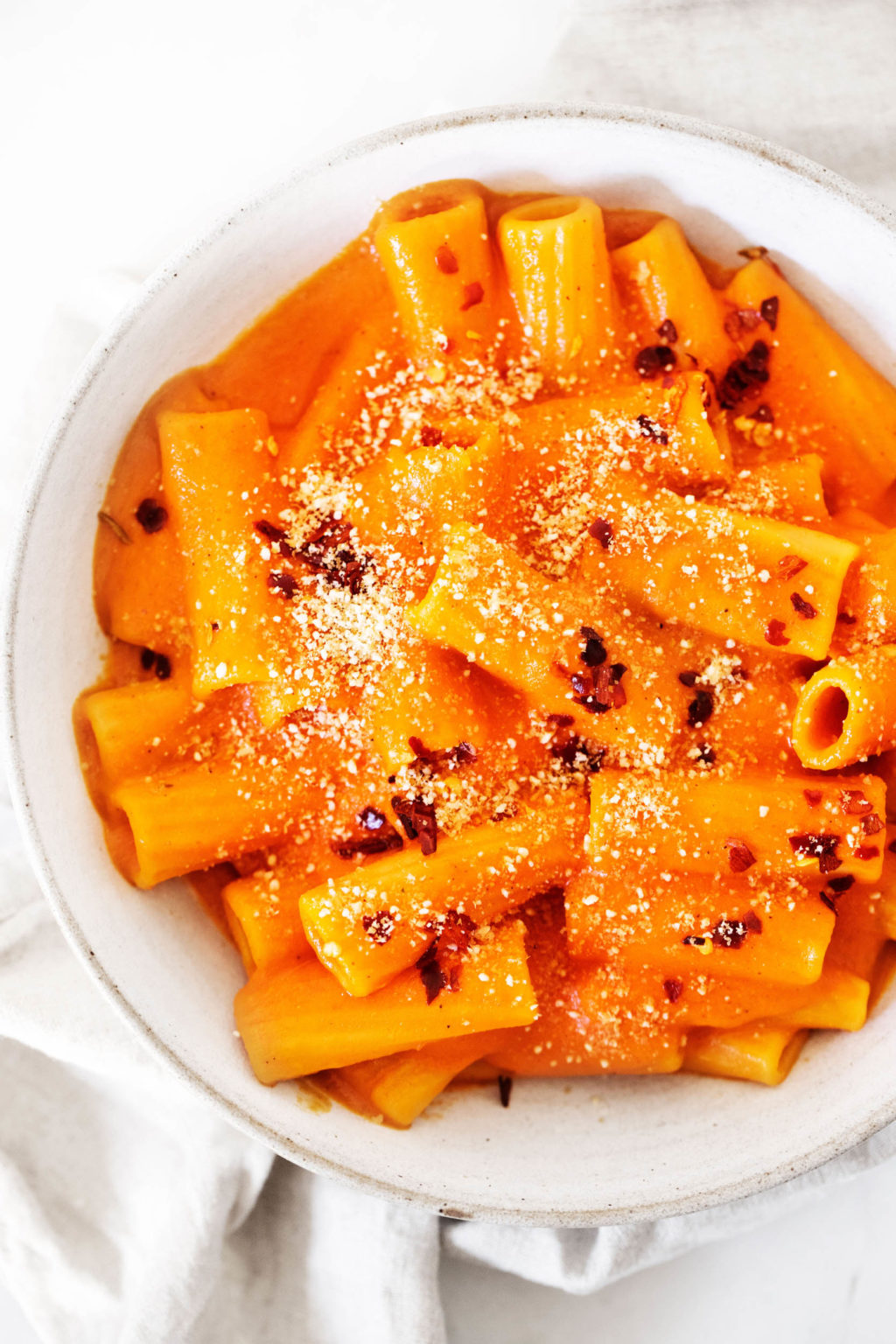 A close up image of a pasta dish with a rich, creamy tomato sauce and crushed red pepper flakes on top.