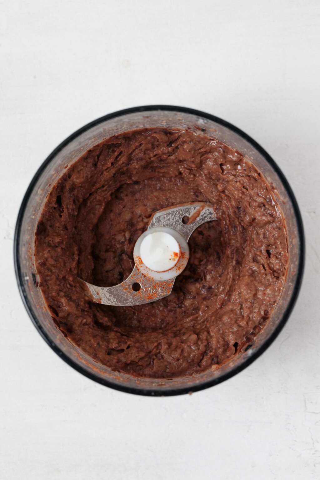 The bowl of a food processor is being used to make a creamy spread with black beans.