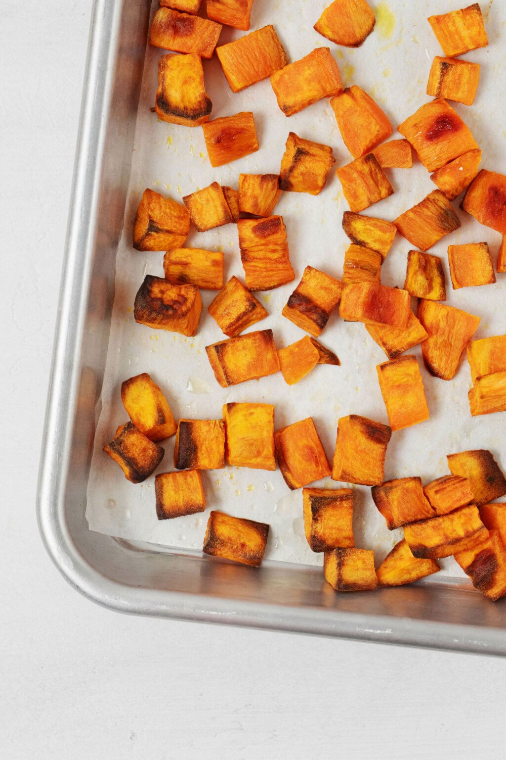 Cubed, roasted sweet potatoes are pictured on a sheet of parchment on a roasting tray.