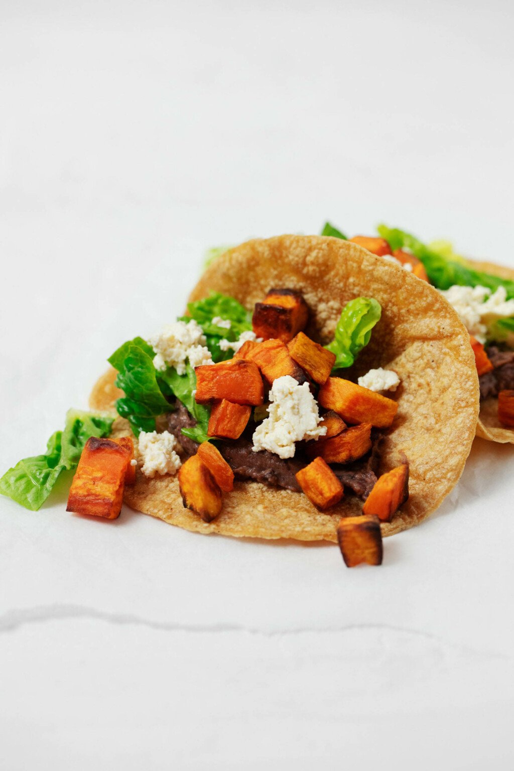 Two tacos, prepared with plant based ingredients, have been laid out on a white sheet of parchment paper.