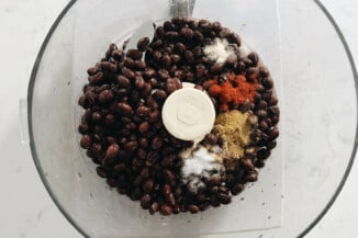 The bowl of a food processor is filled with black beans and other ingredients.