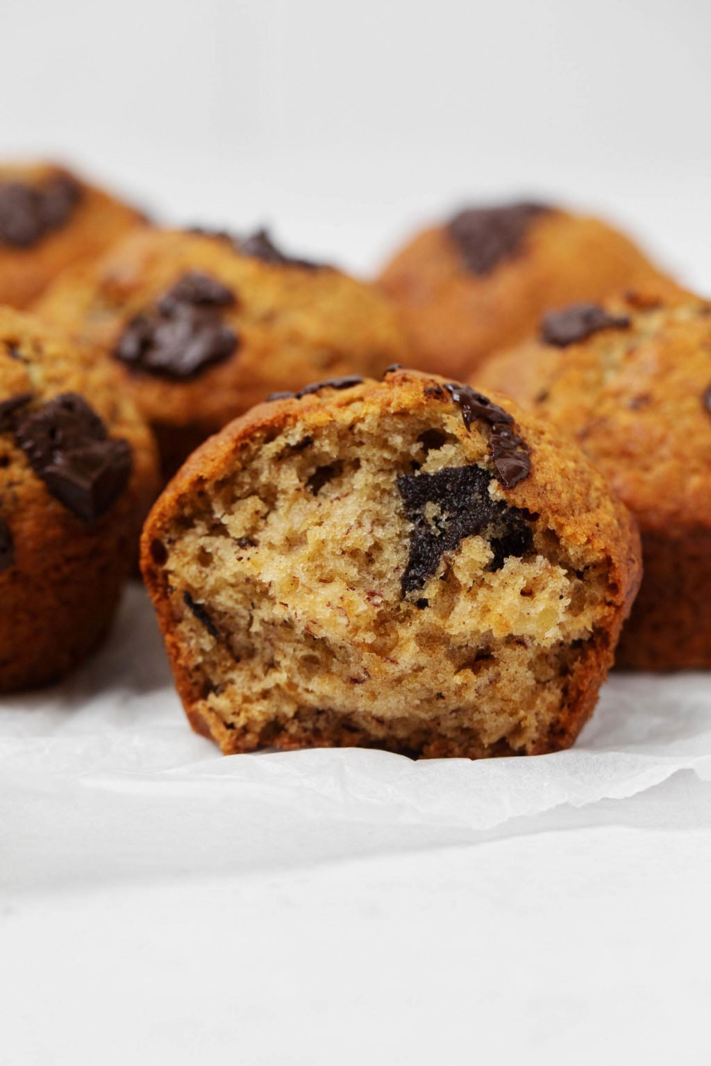 A vegan banana chocolate chip muffin has been broken apart, revealing a soft interior within.