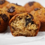 A vegan banana chocolate chip muffin has been broken apart, revealing a soft interior within.