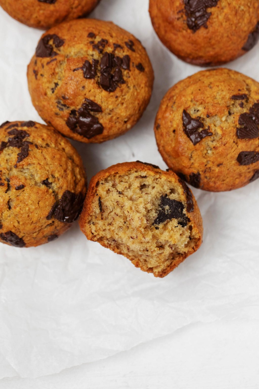 Freshly baked vegan banana chocolate chip muffins are resting on a slice of white parchment paper.