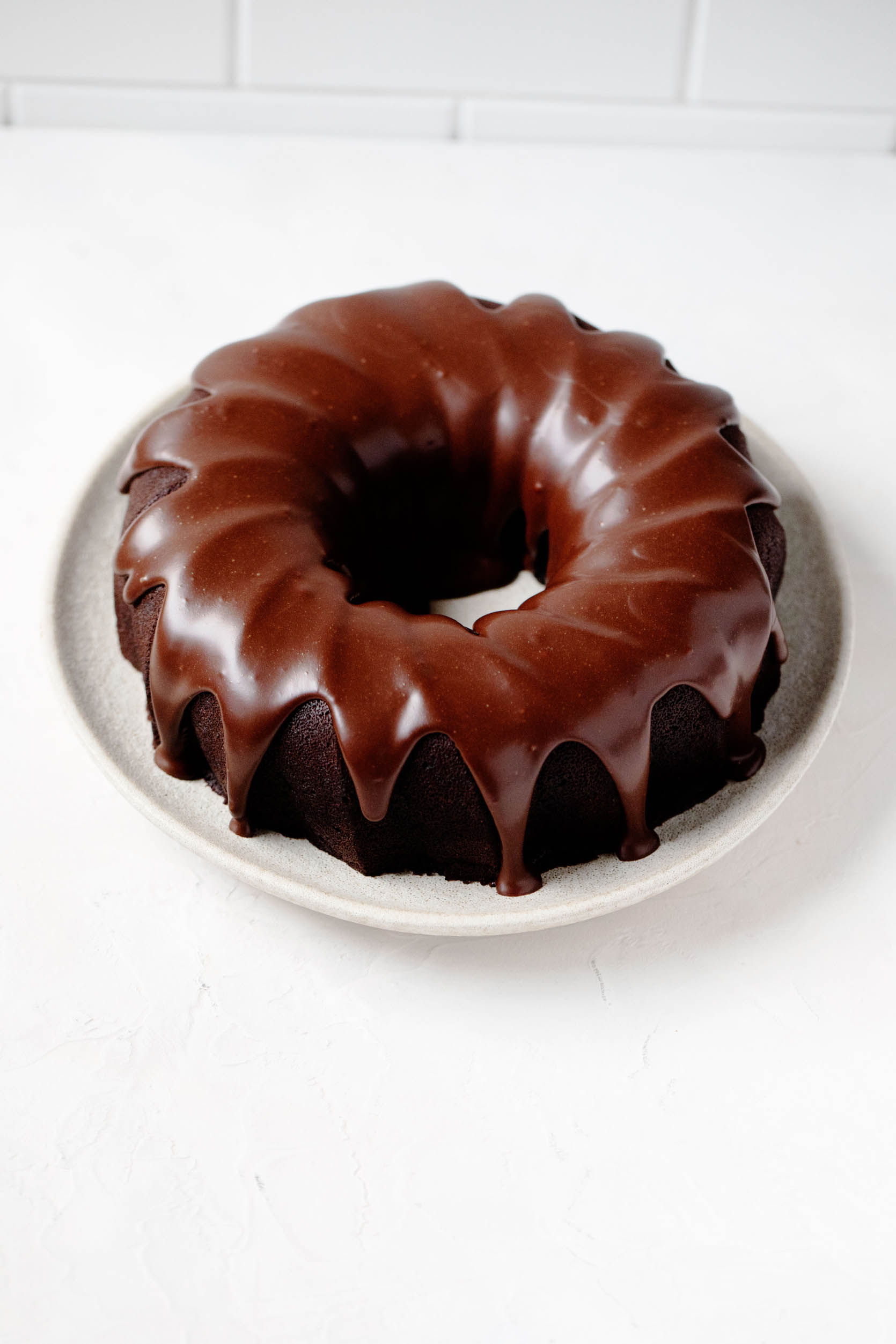 A vegan baked dessert has been recently covered in a glossy, thick glaze. It's resting on a white serving plate.