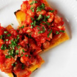 An overhead image of two slices of grilled polenta, which rest on a white dinner plate. They're smothered in a tomato sauce and chickpea mixture.