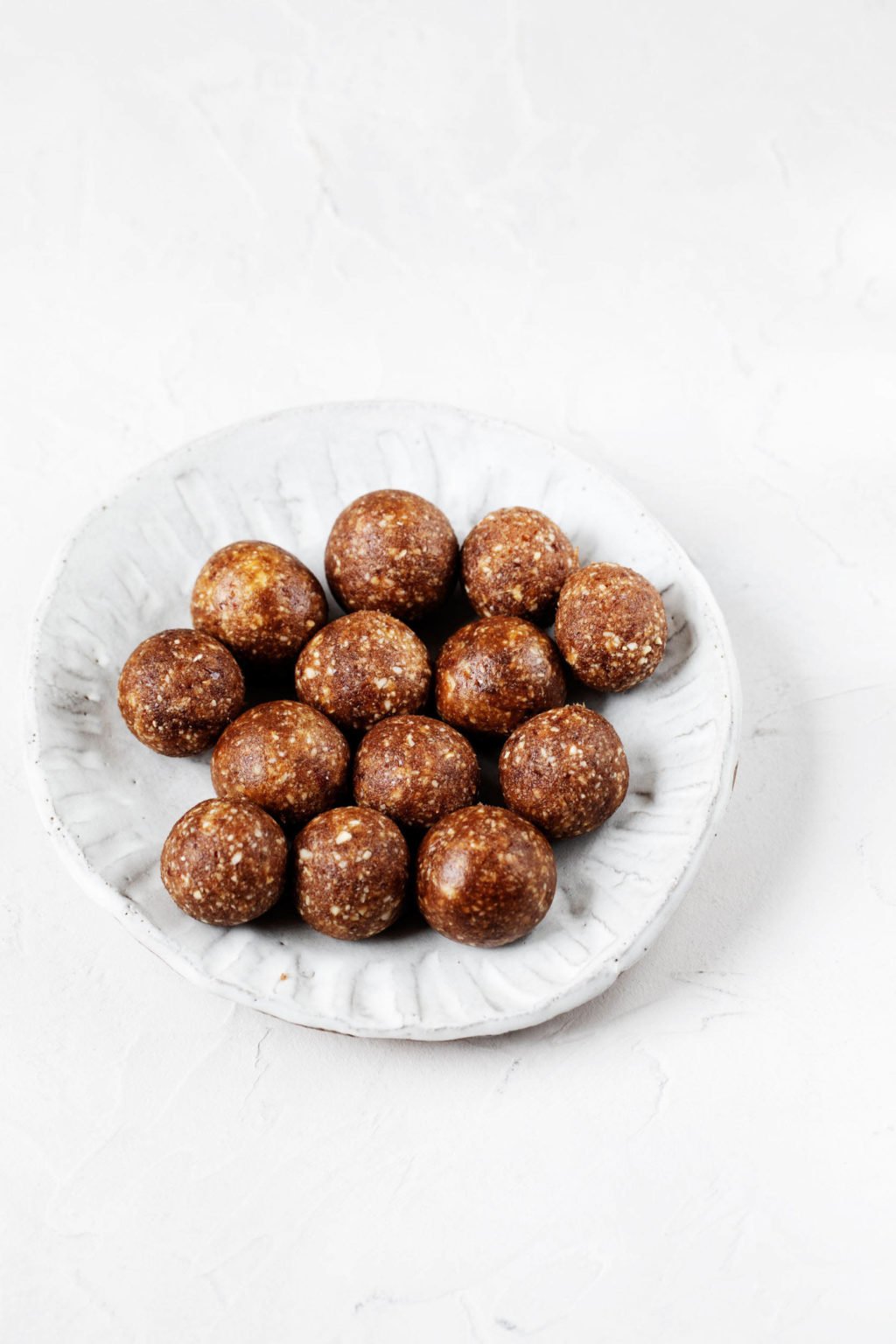 A small, white rimmed plate holds a cluster of vegan energy balls.