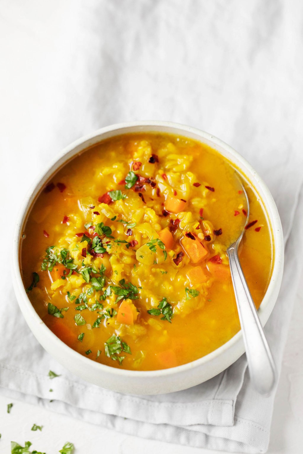 A bowl of vegan cabbage chickpea soup is garnished with bright green parsley. It rests on a gray linen napkin on a white surface.