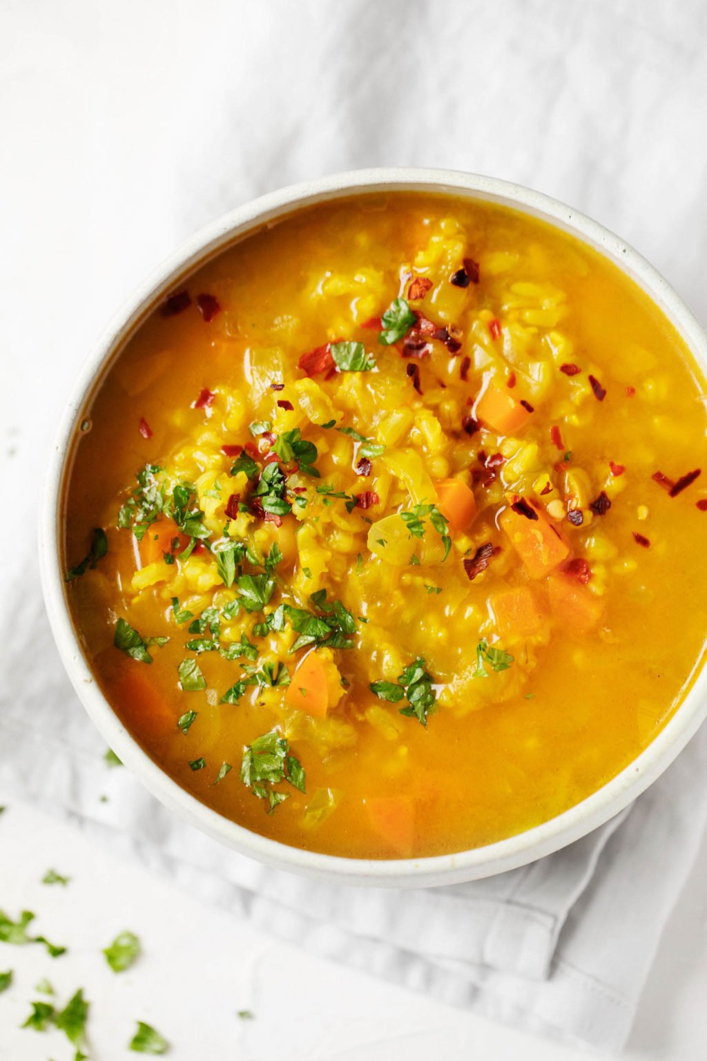 An overhead image of a bowl of vegan soup. It's garnished with chopped herbs and resting on a gray linen napkin.