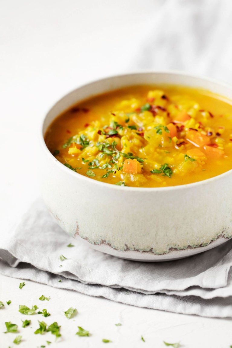 A bowl of spicy cabbage chickpea soup rests on a folded, gray linen napkin.