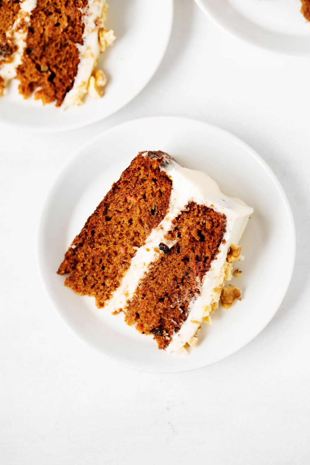 A neat slice of vegan carrot cake has been placed on a small dessert plate. Another slice peeks out in the background.