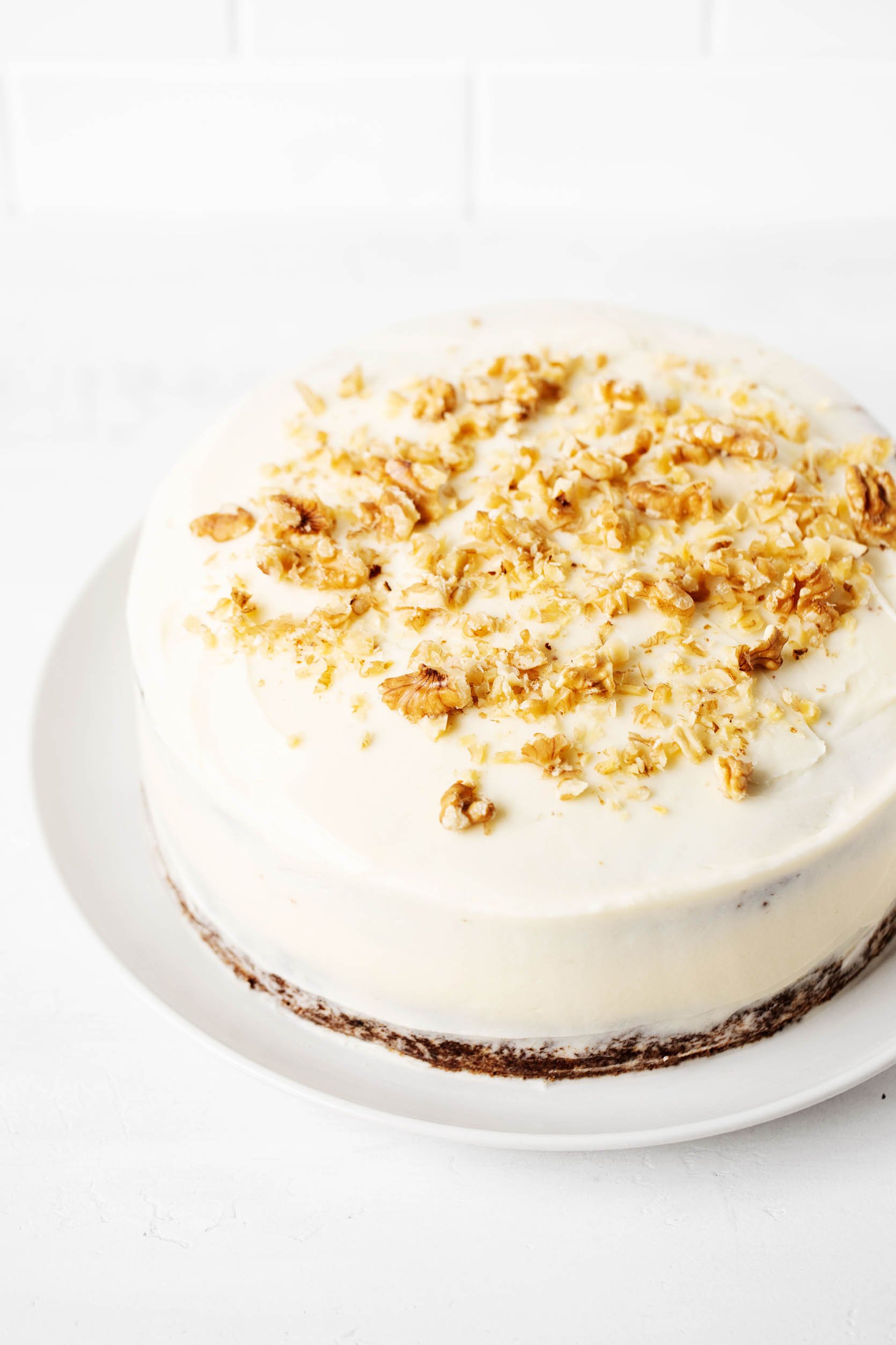A frosted vegan carrot cake with chopped walnuts on top.