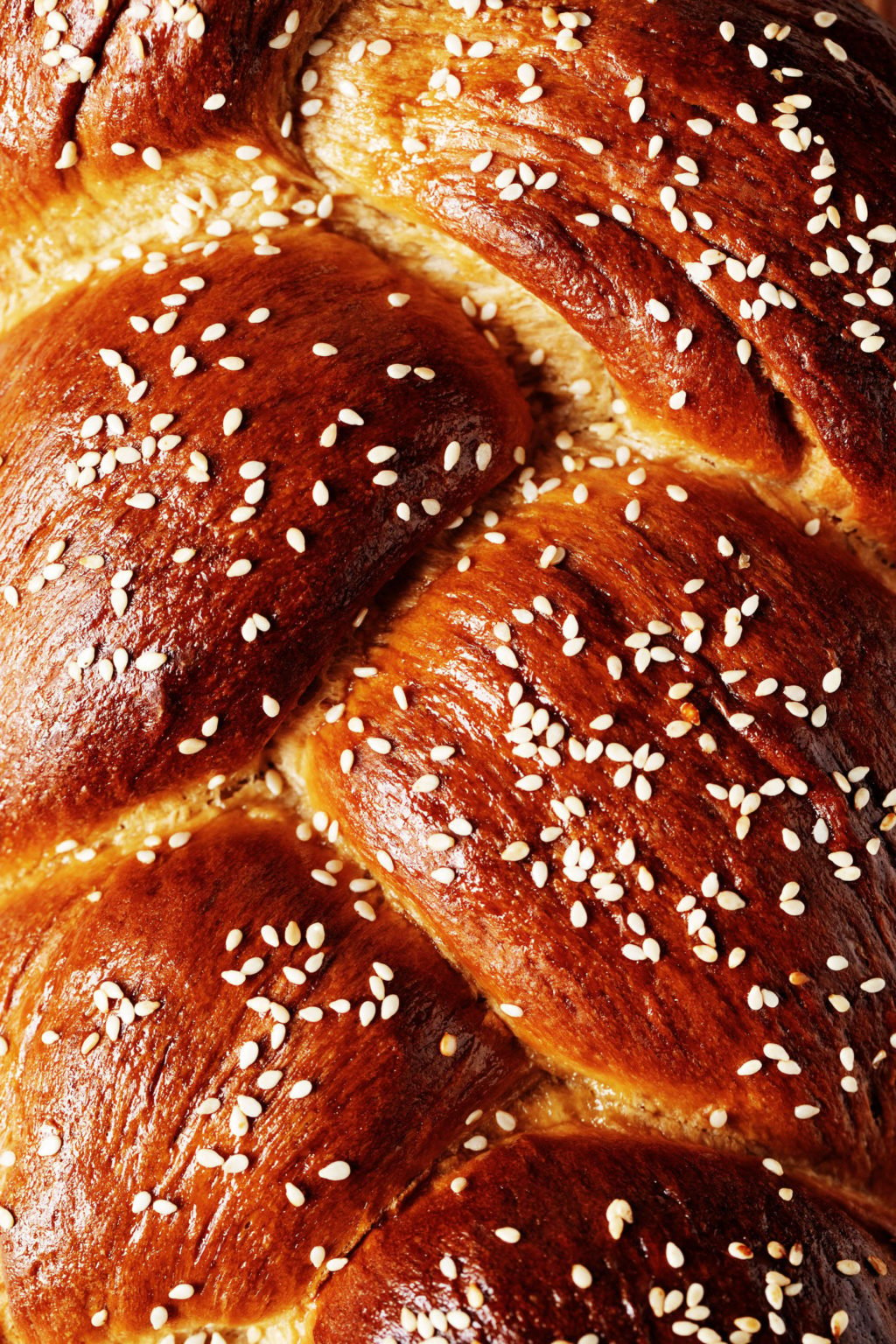 A close up, overhead image of a deep brown, baked and braided loaf of bread. It has been topped with sesame seeds.