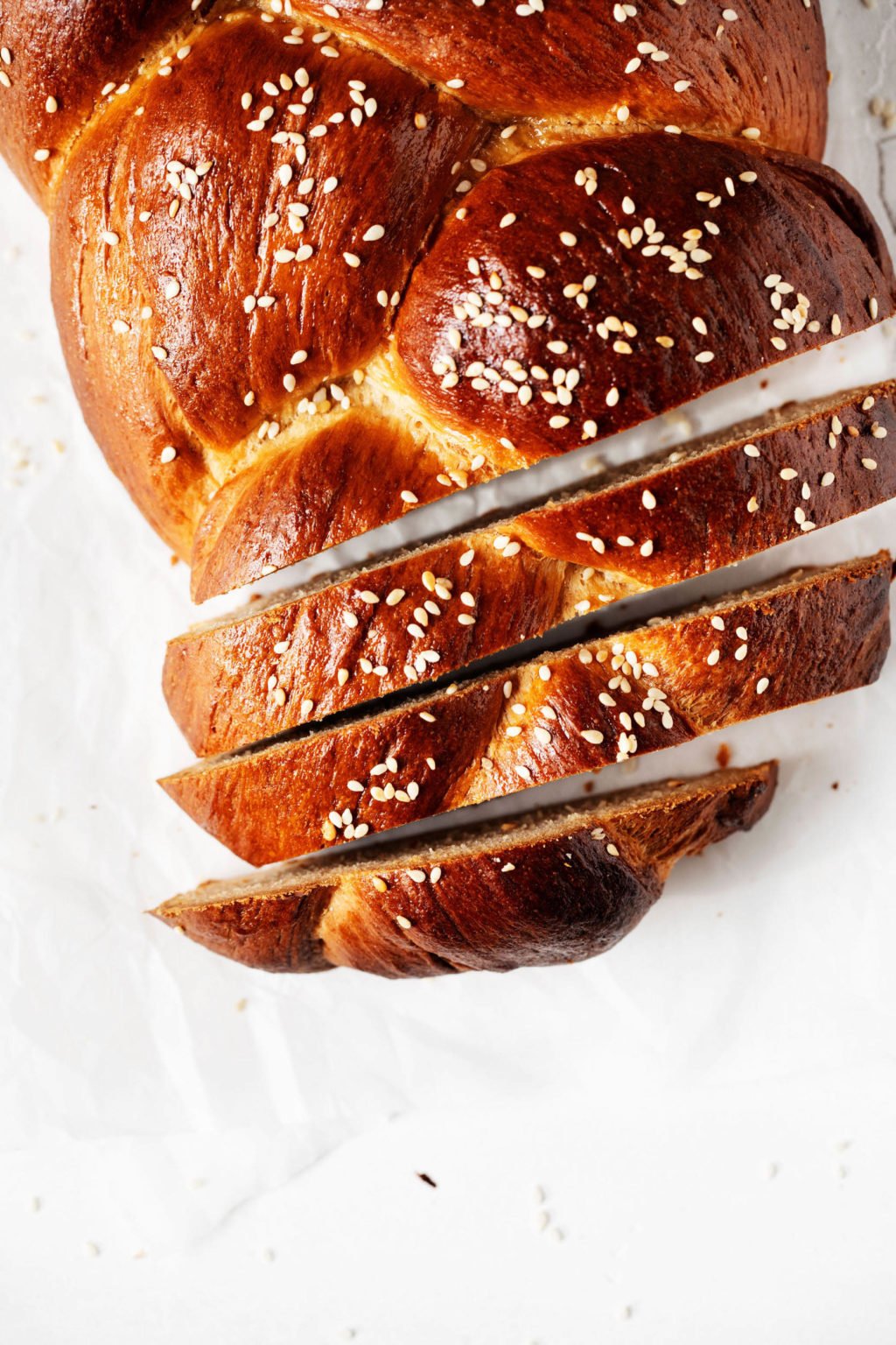 An overhead image of a braided vegan Tsoureki sweet bread, which has been sliced on top of white parchment paper.