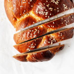 An overhead image of a braided vegan Tsoureki sweet bread, which has been sliced on top of white parchment paper.