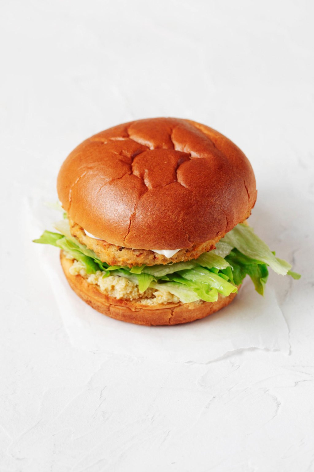 A vegetable based burger is served on a fluffy burger bun. It rests on a white sheet of parchment.