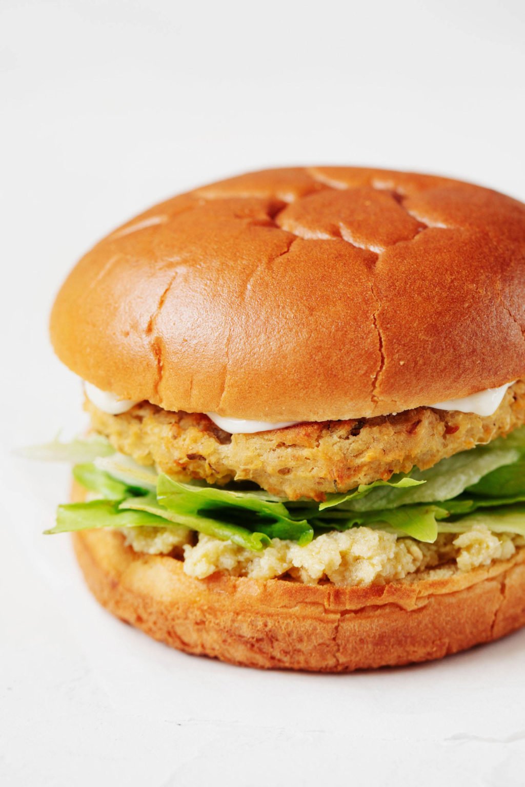 A close-up photograph of a plant-based patty, served on a fluffy bun with lettuce and a creamy spread.